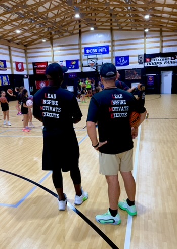 Two LIME coaches watching a youth basketball camp from the court