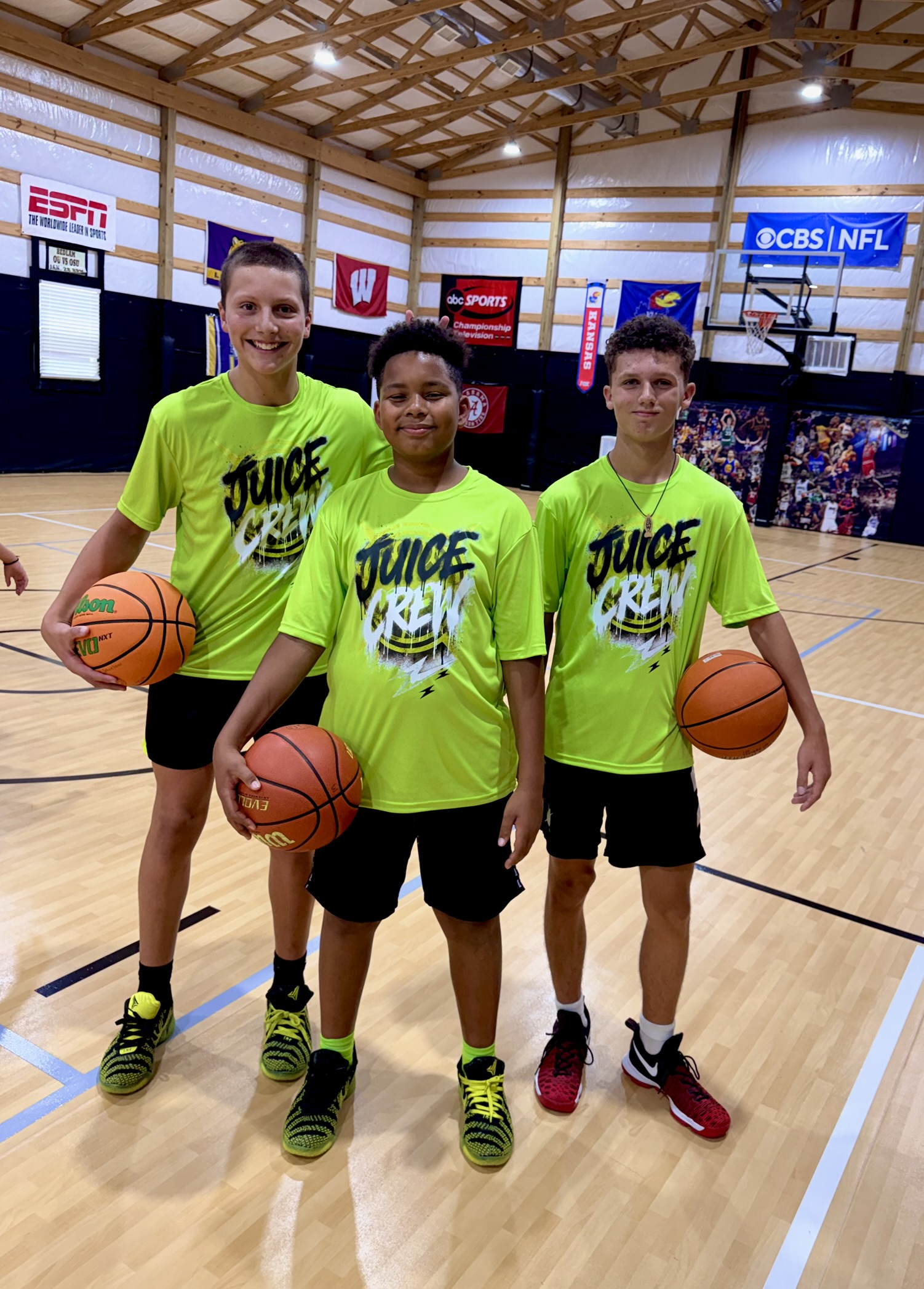 Three young basketball players in bright Juice Crew shirts holding basketballs