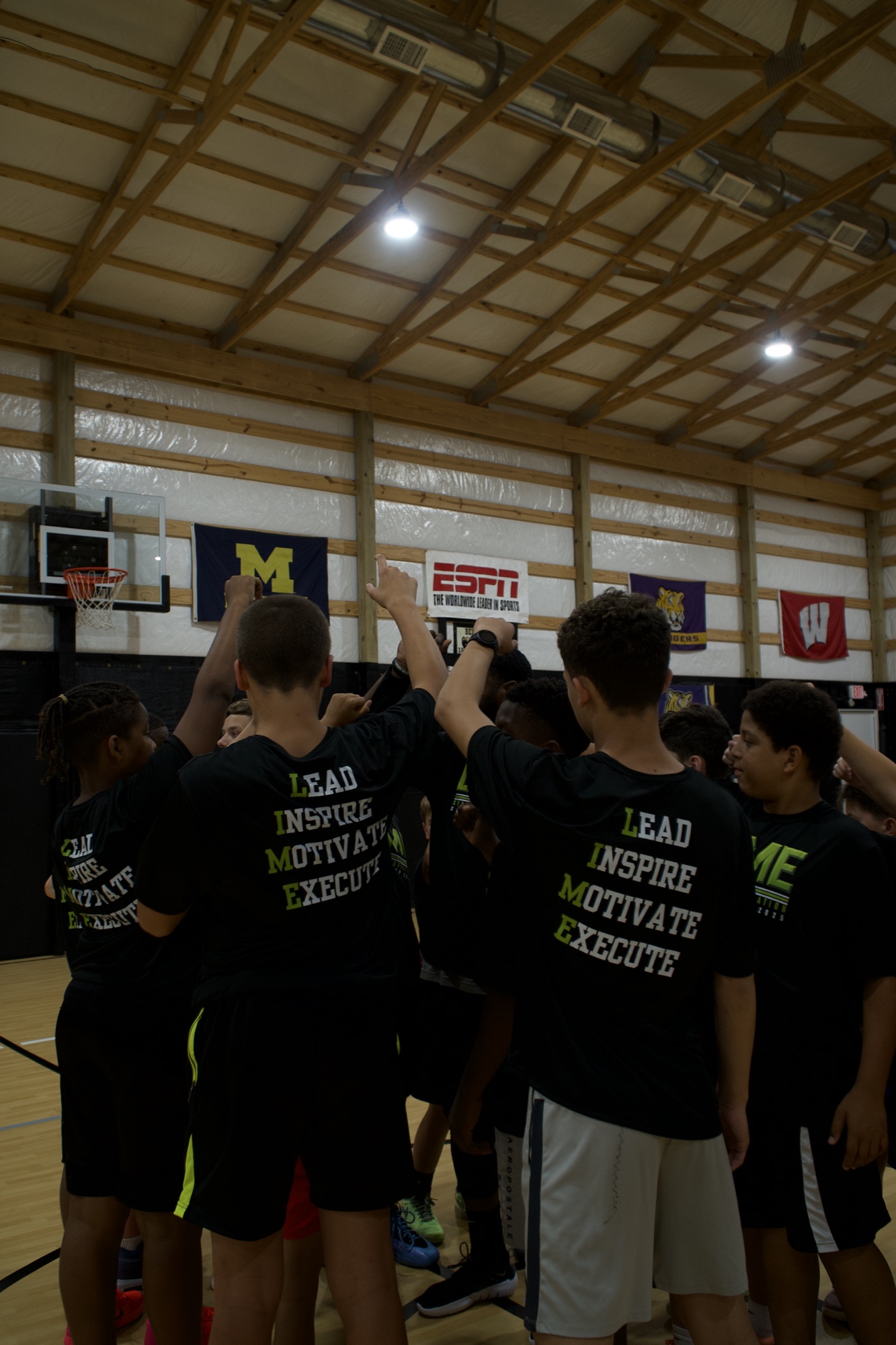 Young LIME athletes raising their hands together in a basketball camp huddle